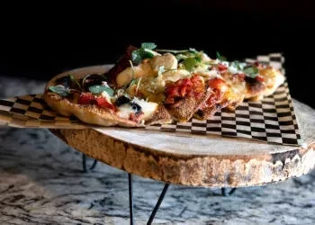 Several bruschetta pieces with tomatoes, cheese, and herbs on rustic wood.