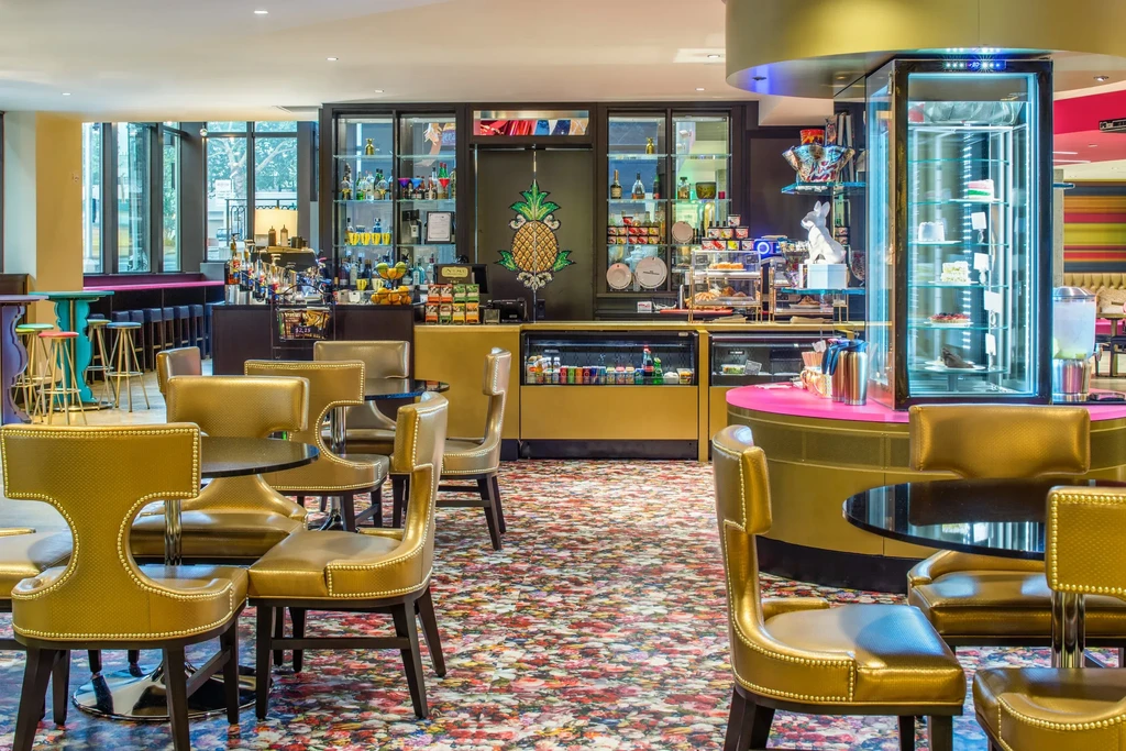 Modern restaurant interior, gold chairs, colorful carpet, dessert counter, pineapple motif.