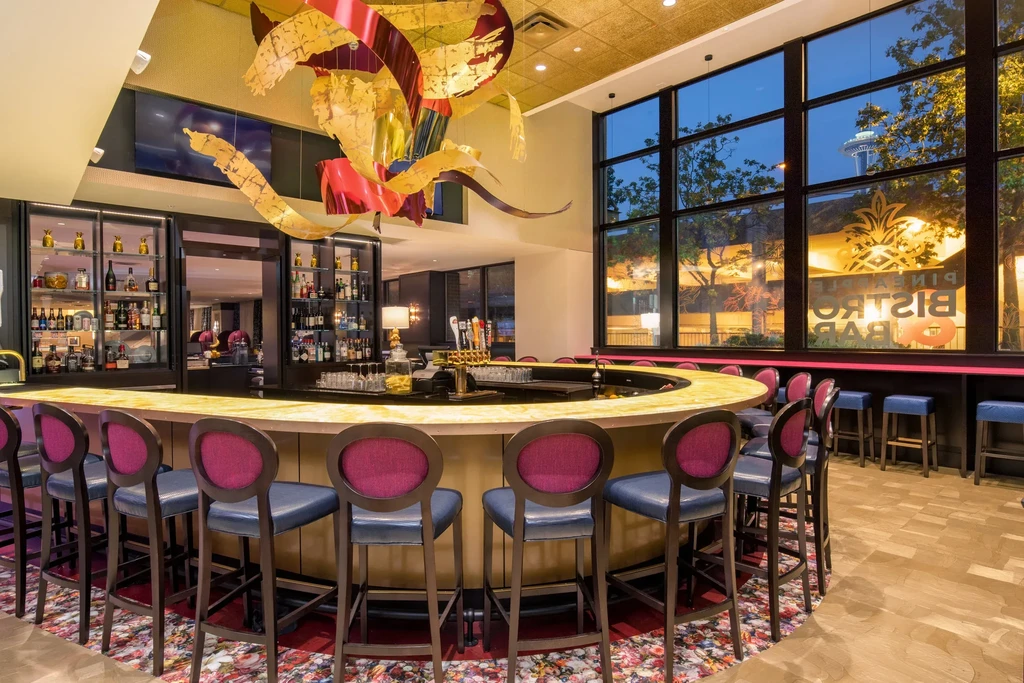 Semi-circular bar, colorful stools, chandelier, and Space Needle cityscape view.
