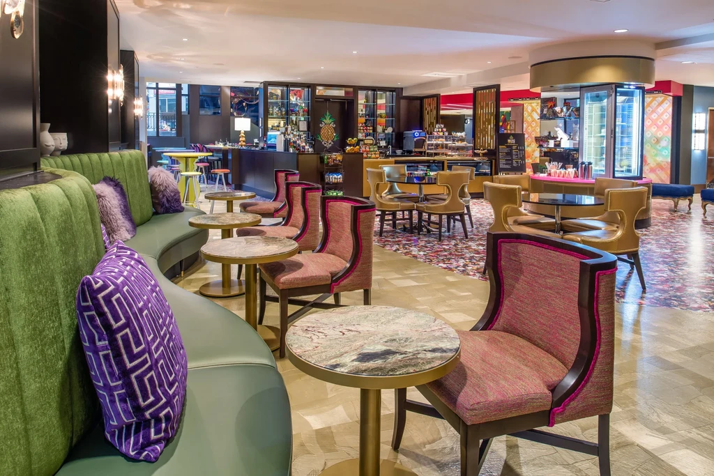 Vibrant, eclectic lounge with olive sofa, colorful seating, and pineapple bar.