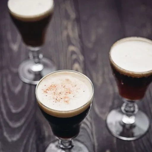 Three stemmed dark drinks with spiced foam on a wooden table.
