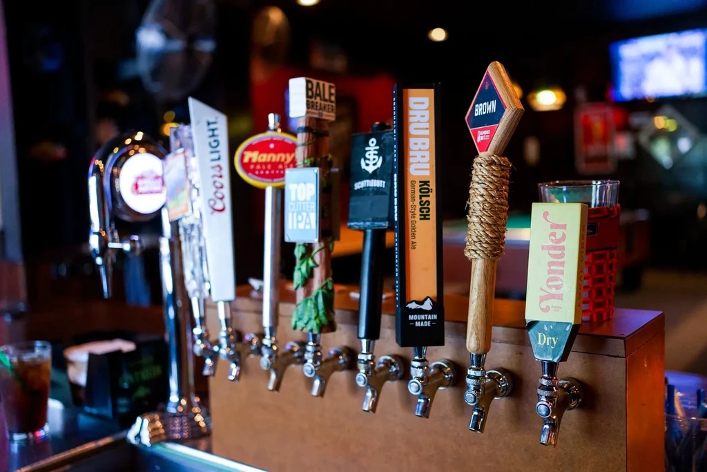 Row of unique beer tap handles with legible brands at a bar.
