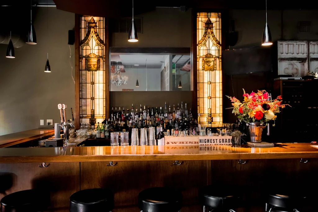 Elegant dark wood bar with liquor, stained glass, and pendant lights.