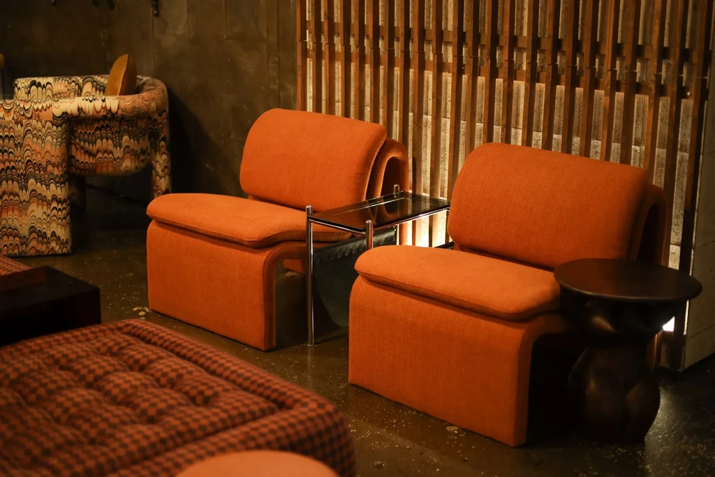 Two modern burnt orange armchairs in a dimly lit lounge.