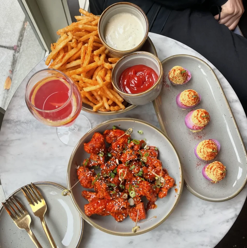 Red-sauced chicken, fries, and purple deviled eggs on a table.