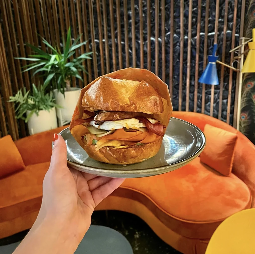 Hand holding a brioche breakfast sandwich with egg and bacon.