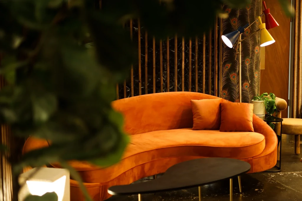 Orange velvet sofa, peacock wallpaper, and colorful lamp in a lounge.