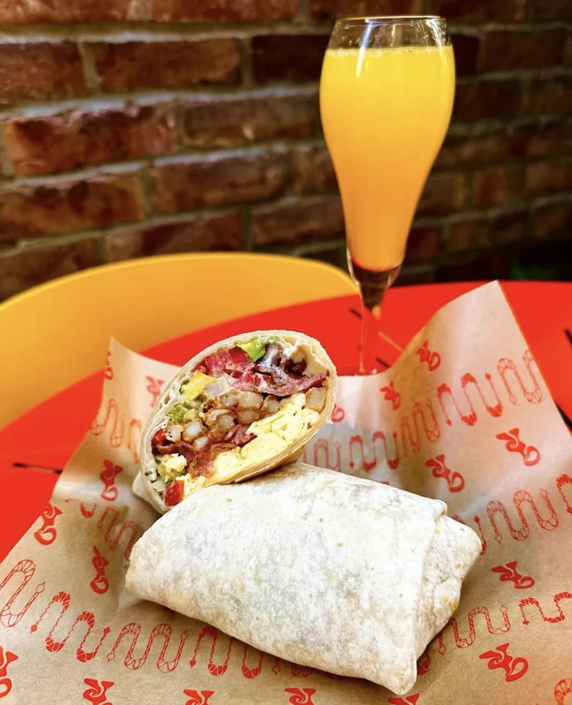 Two burritos, one halved with eggs, bacon, potatoes, and orange juice.
