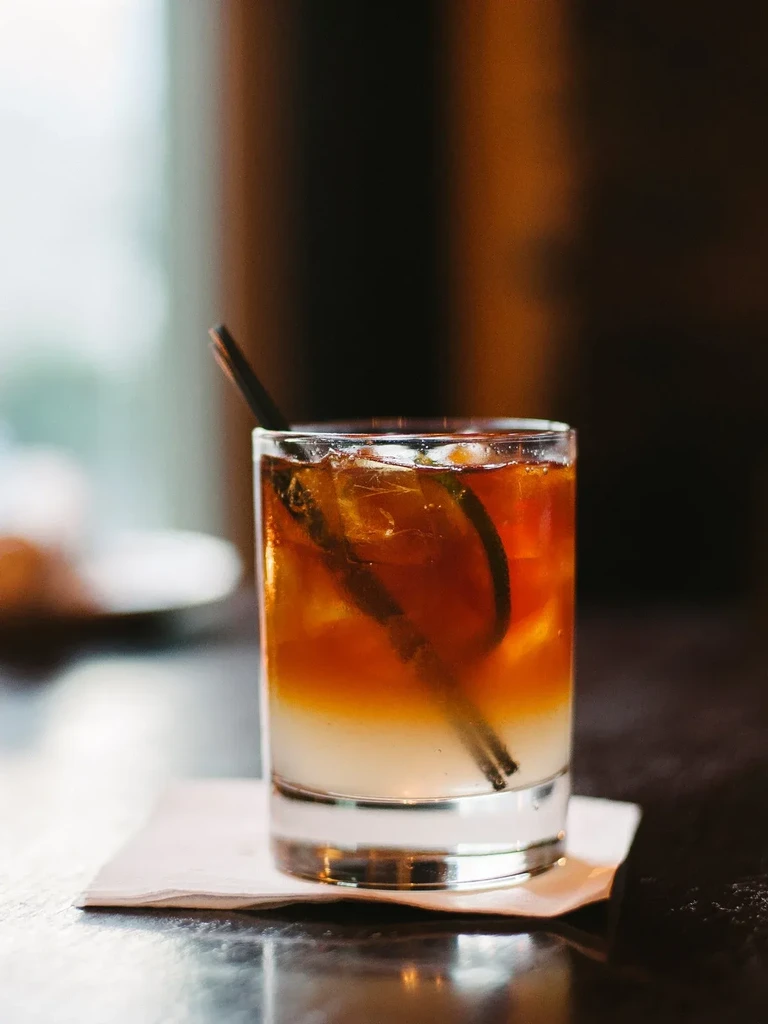 Layered amber and creamy cocktail with ice, straw, and lime garnish.