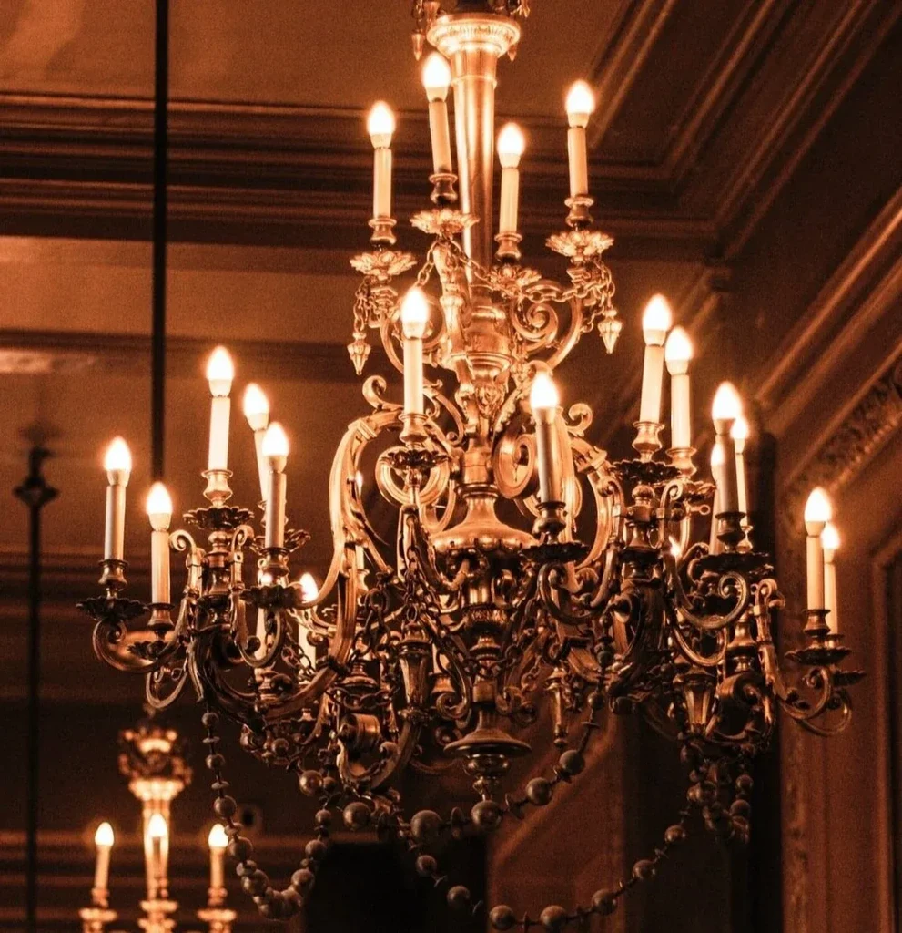 Intricate gold chandelier with glowing candle-flame bulbs in a grand room.