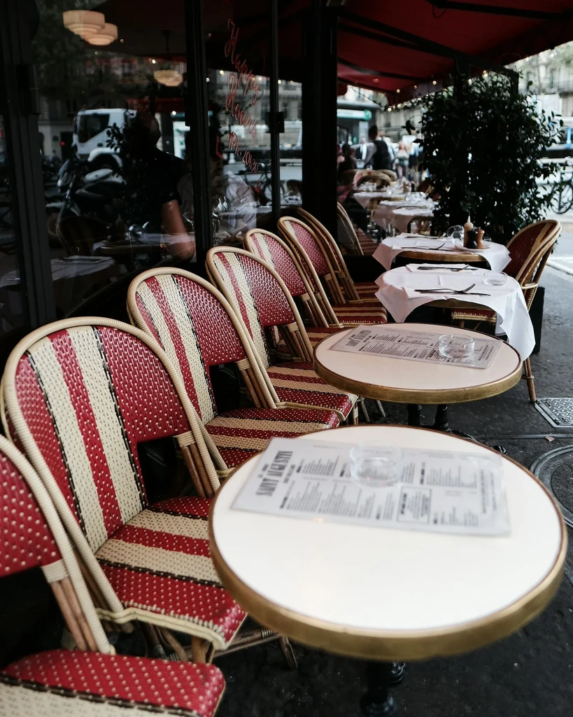 Outdoor cafe with empty striped chairs, white tables, red awning.
