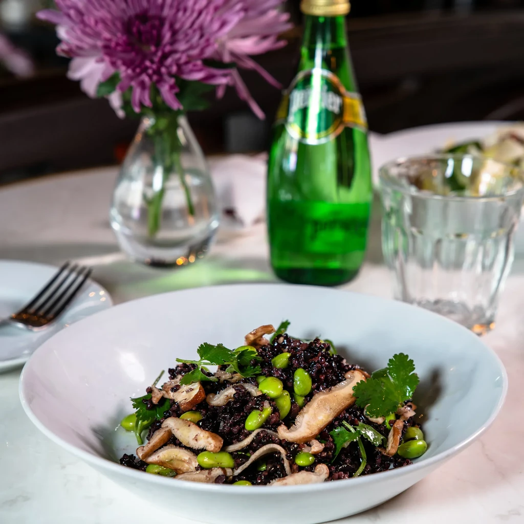 White bowl of black rice, green edamame, mushrooms, and cilantro.