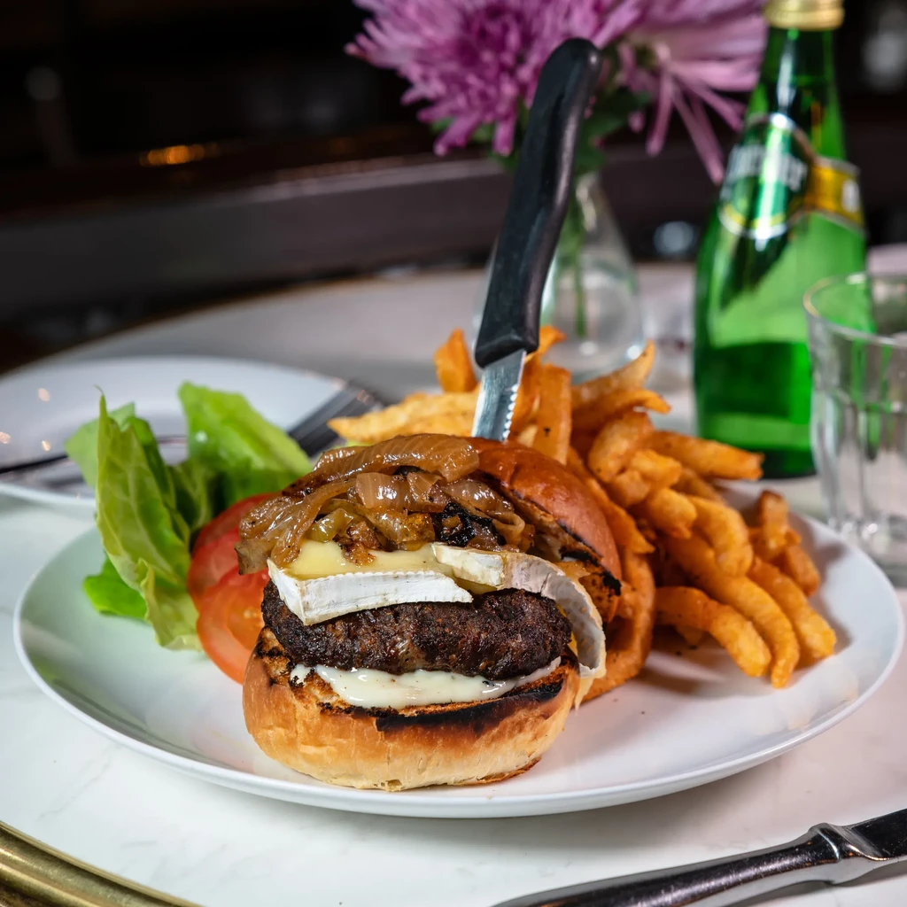 Gourmet burger with brie, fries, lettuce, and tomato on white plate.