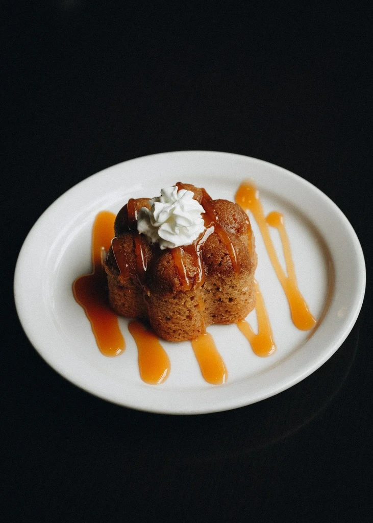 Brown dessert with caramel sauce and whipped cream on white plate.