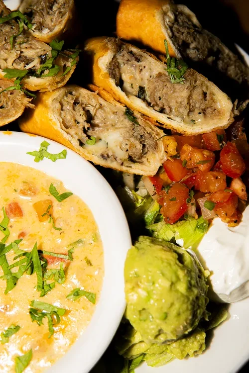 Golden-brown rolls filled with meat and cheese, with guacamole and dips.