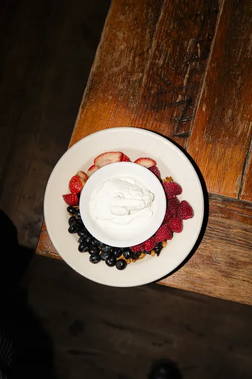 Overhead berry yogurt parfait with granola in white bowl on wood.
