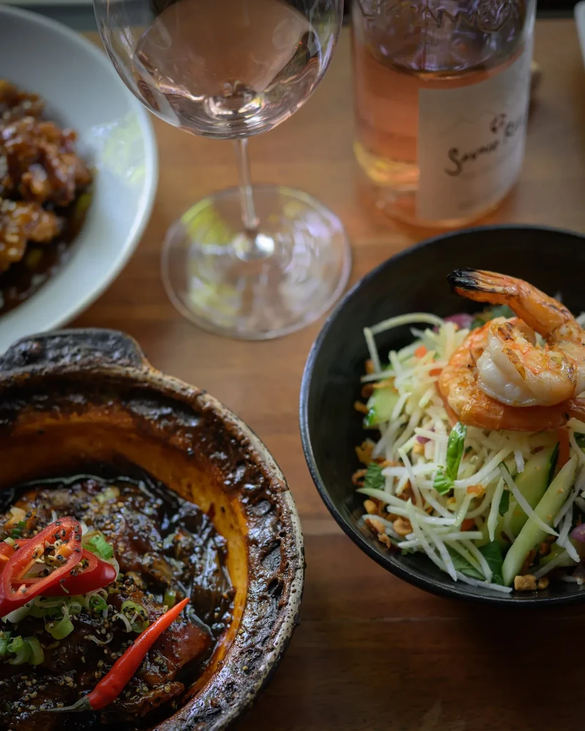 Dark-sauced stew, shrimp salad, and rosé wine on a wooden table.
