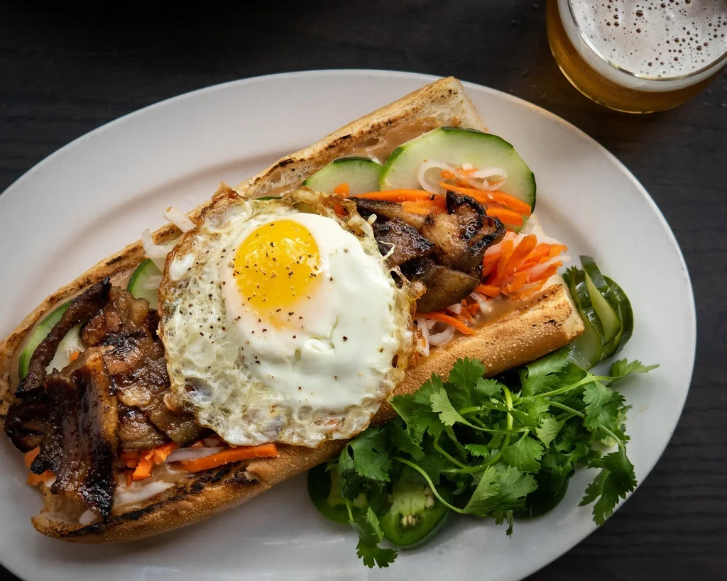 Overhead shot of a Banh Mi sandwich with fried egg and beer.