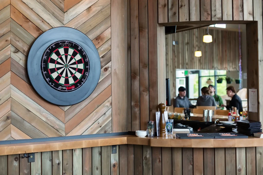 Colorful dartboard on a chevron wooden wall, with a bar counter.