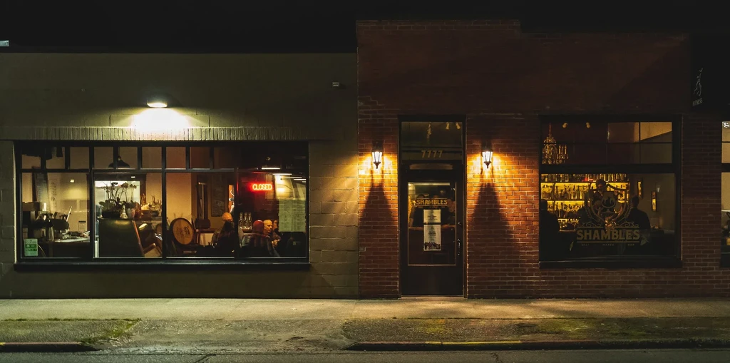 Night photo of a "CLOSED" coffee shop next to "SHAMBLES" bar.