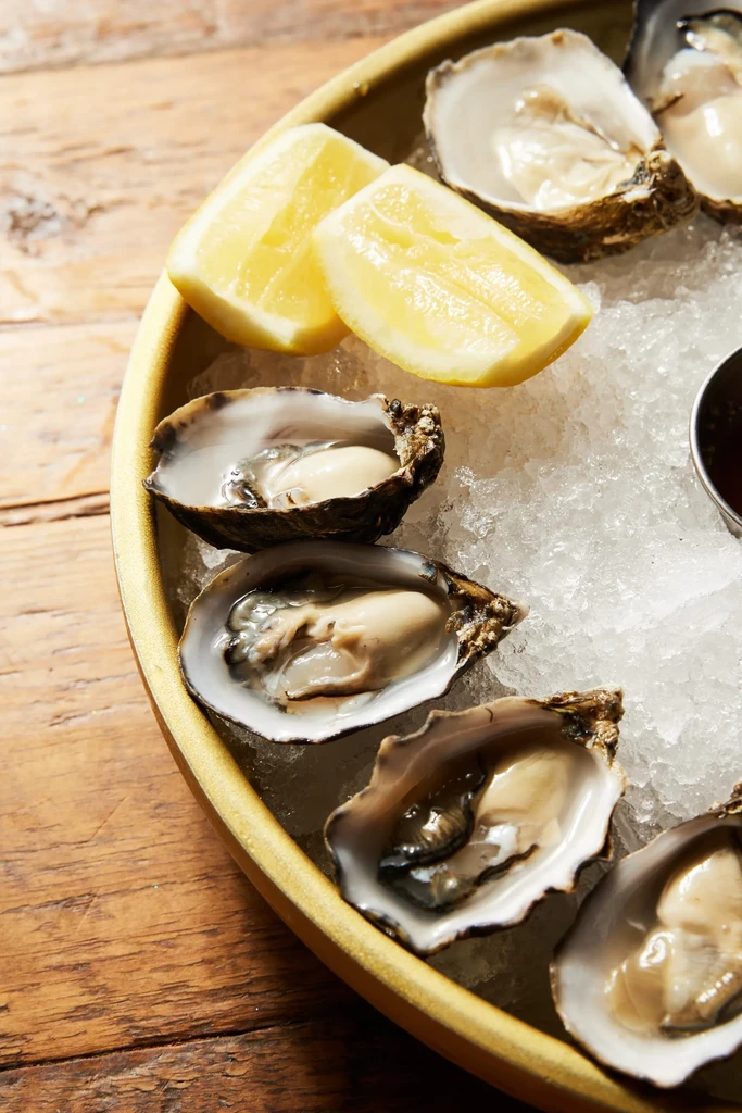 Fresh shucked oysters on ice with lemon slices and dipping sauce.