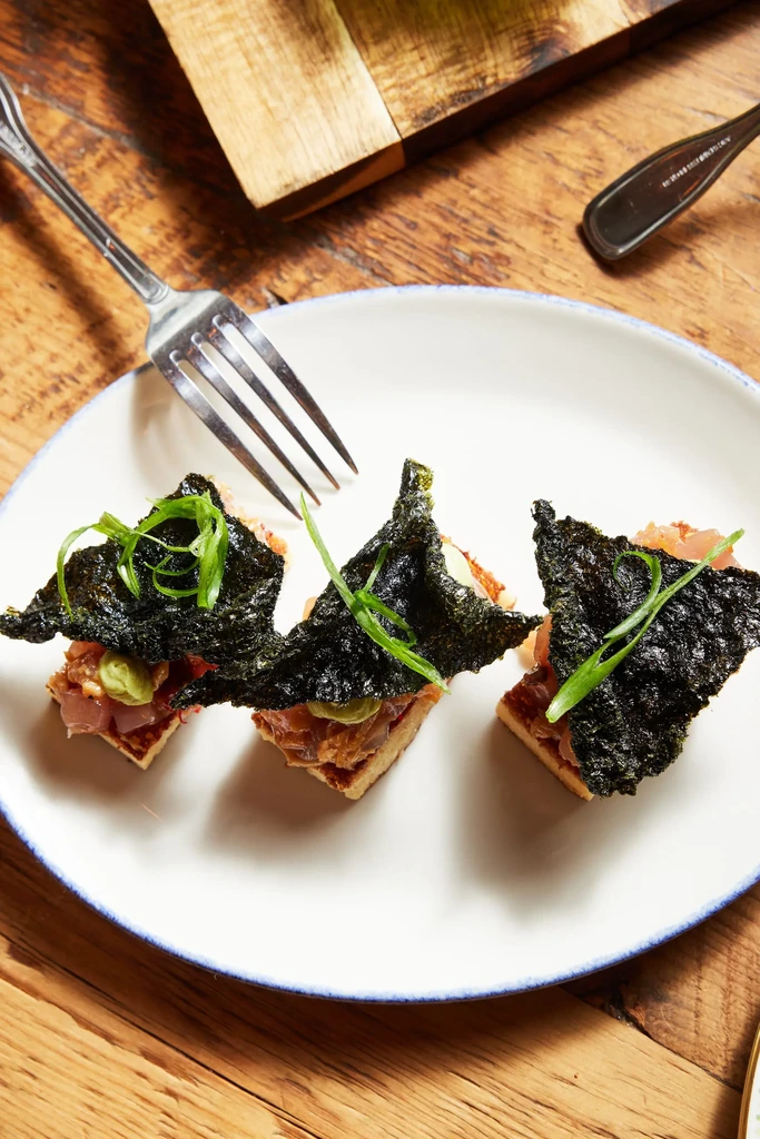 Three rectangular tartare appetizers with nori and greens on a white plate.