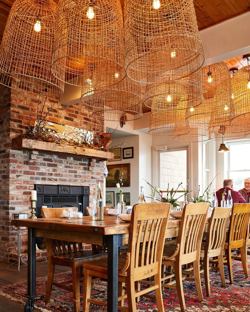 Prominent woven lights above a rustic dining table and brick fireplace.