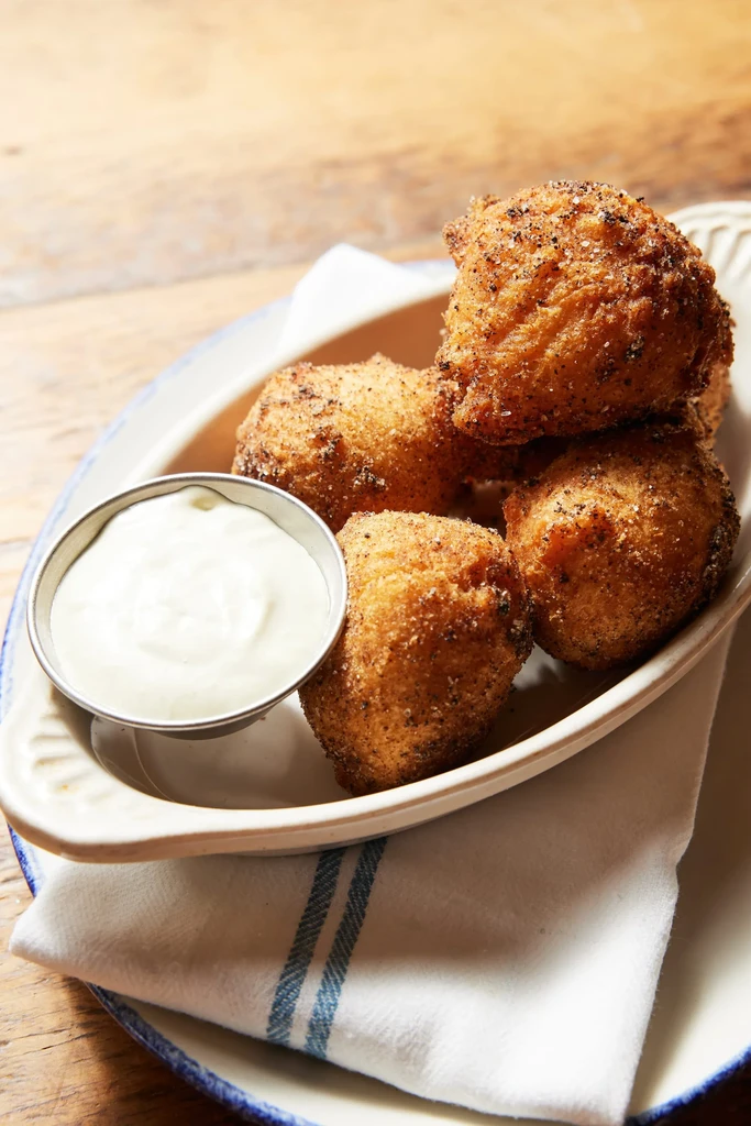 Five round, golden fried food items and sauce on a wooden table.