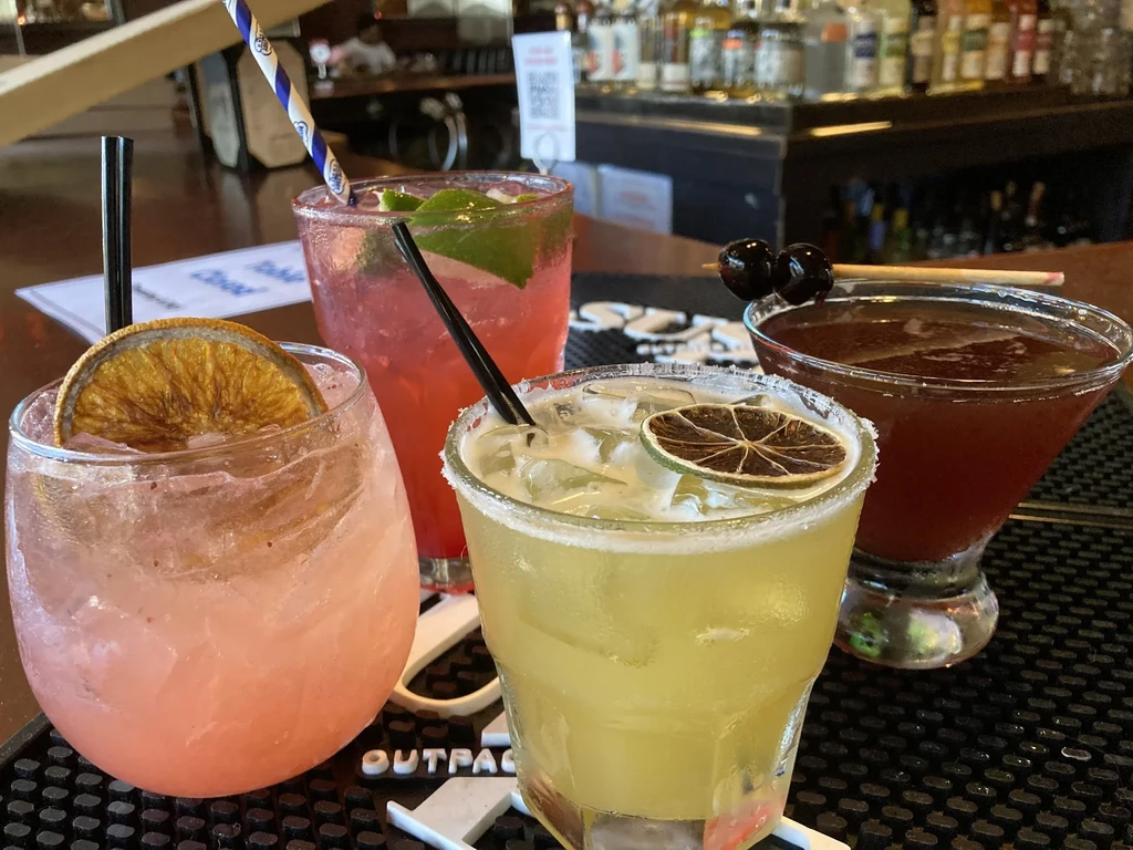 Four colorful cocktails with ice and garnishes on a bar mat.