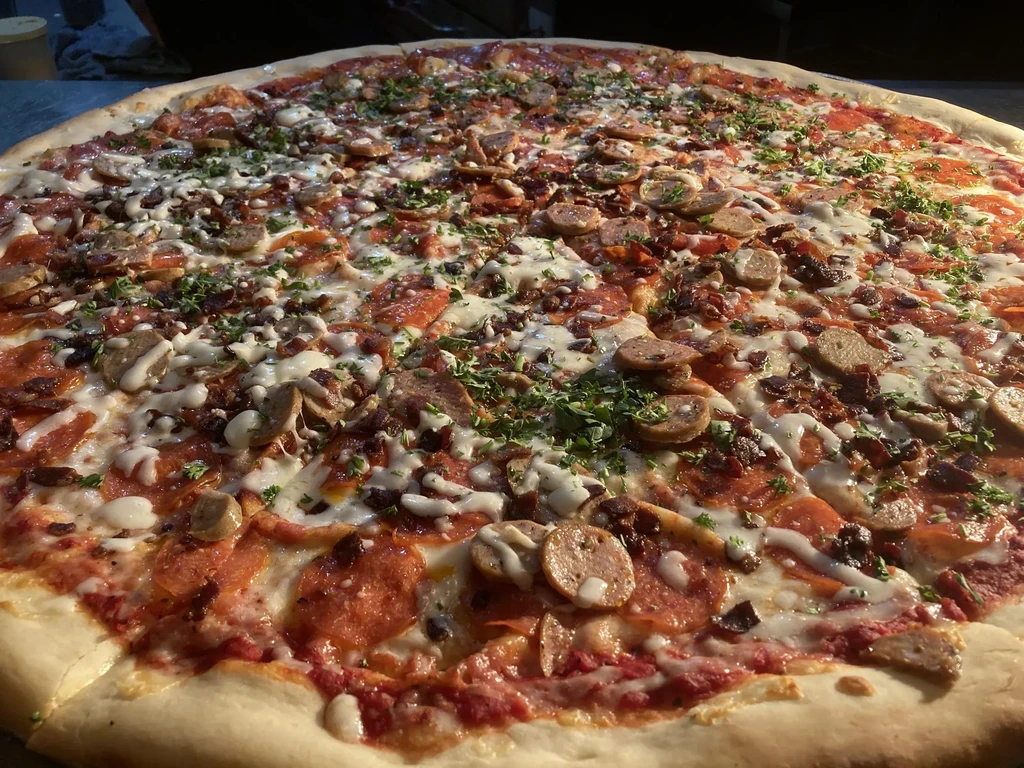 Generously topped pizza with pepperoni, sausage, melted cheese, and fresh herbs.