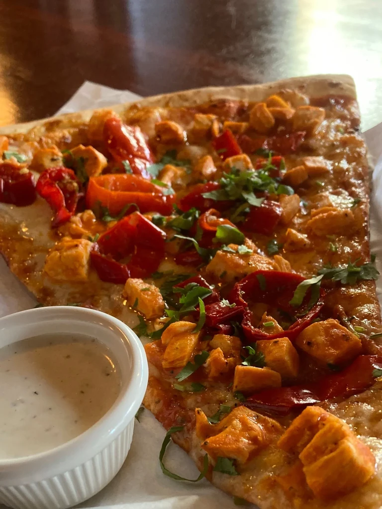 Golden-crusted chicken pizza slice with peppers, herbs, and dipping sauce.