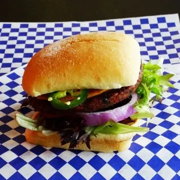 Close-up burger with jalapeños, red onion, and lettuce on checkered paper.