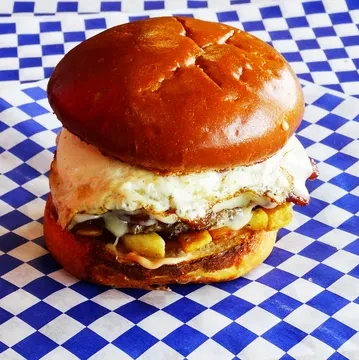 Brioche burger with meat patty, fries, melted cheese, and fried egg.