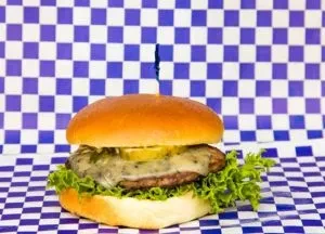 Hamburger with melted blue cheese, lettuce, pickles, blue skewer, checkerboard.