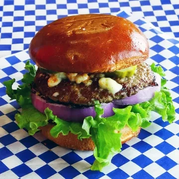 Close-up of a brioche burger with blue cheese, pickles, onion, lettuce.