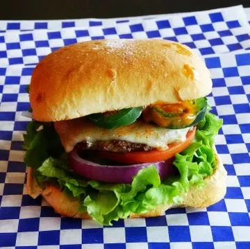Fresh burger with lettuce, tomato, cheese, jalapeños, on checkered paper.