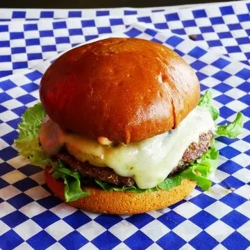 Thick cheeseburger with melted cheese and lettuce on checkered paper.