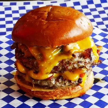 Multi-patty cheeseburger with melted cheese, bacon, and green toppings.