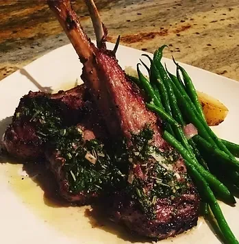 Two herb-crusted lamb chops, green beans, and roasted potato on a plate.