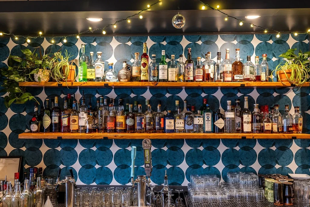 Well-stocked bar with liquor bottles, plants, glassware, and festive decor.