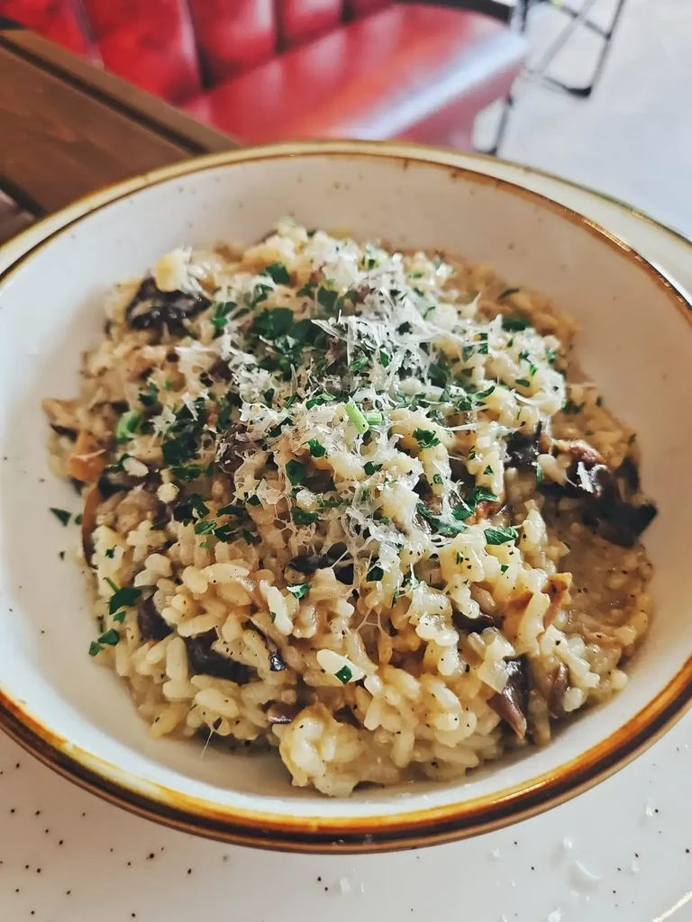 Creamy mushroom risotto, garnished with Parmesan cheese and green herbs.