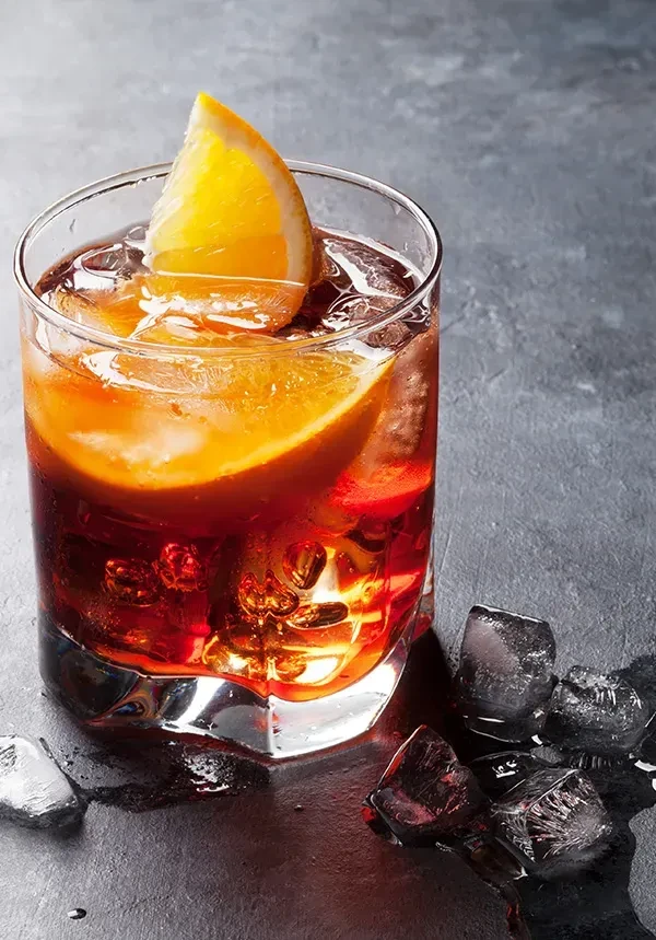 Amber-red cocktail in old-fashioned glass with orange and melting ice.
