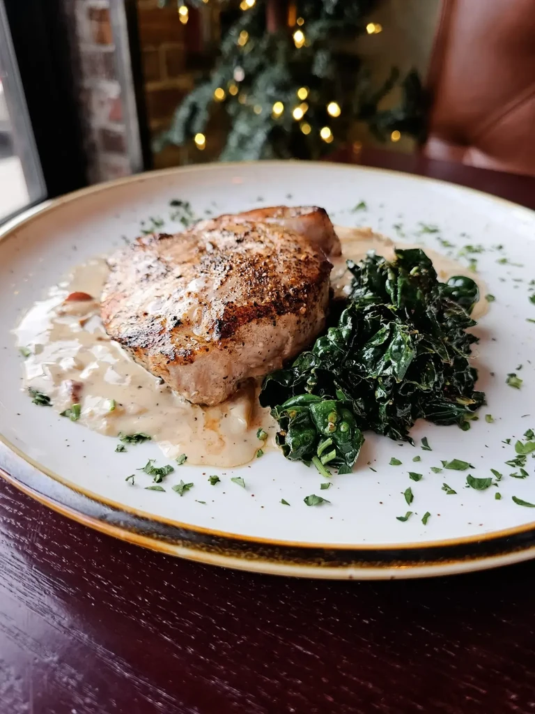 Seared meat with creamy sauce, sautéed greens, and fresh herbs.