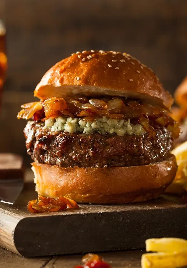 Gourmet hamburger with blue cheese and caramelized onions on wooden board.
