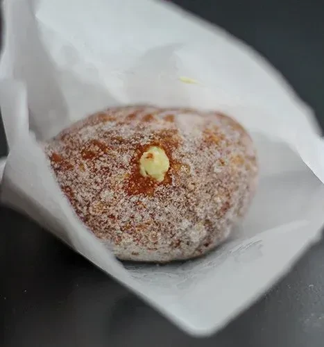 Sugar-coated pastry with yellow cream filling on crumpled white paper.
