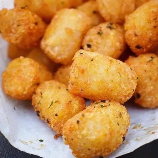 Golden-brown fried potato tots dusted with herbs and pepper in a white liner.