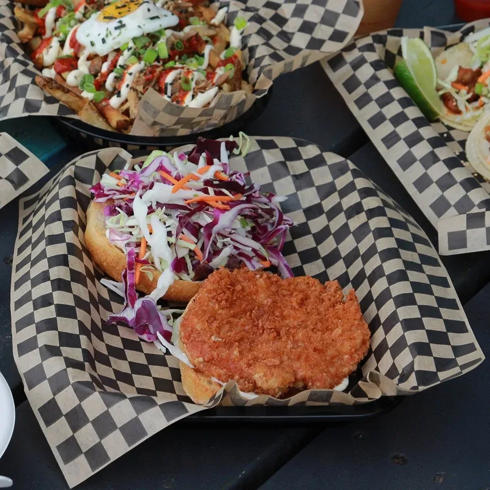 Open-faced sandwich, coleslaw, breaded patty, loaded fries, tacos on dark surface.