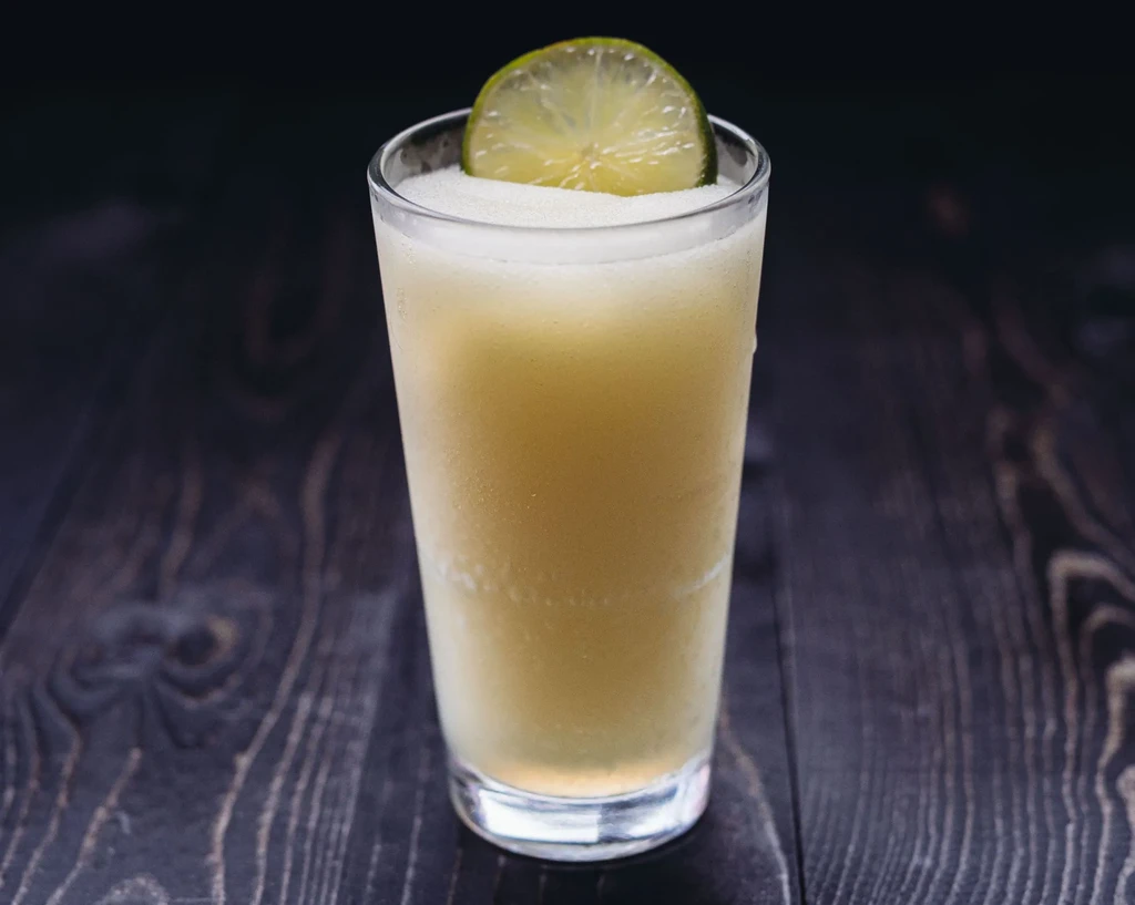 Frozen yellow drink in a glass with a lime on wood.