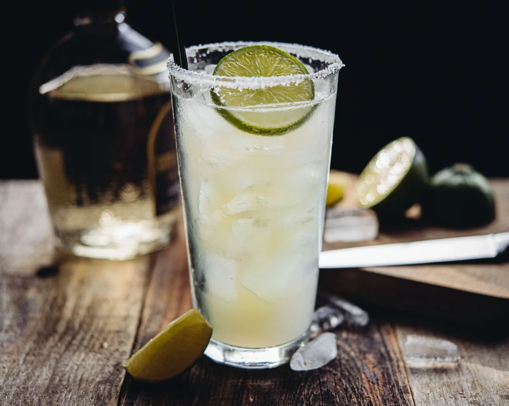 Pale green margarita with lime, salted rim, and ice on a wooden surface.