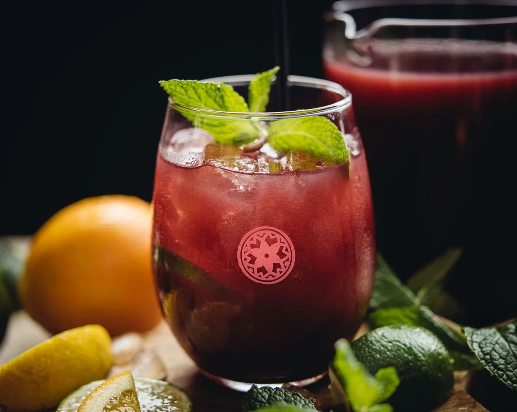 Iced reddish-purple drink with mint, citrus, and straw on wood.